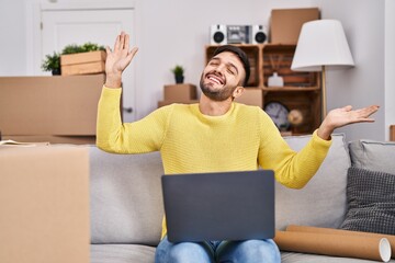 Canvas Print - Young hispanic man using laptop stretching arms at new home