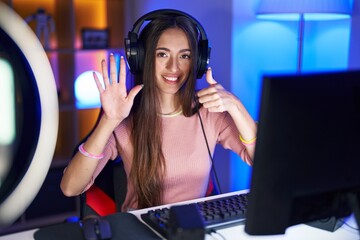 Wall Mural - Young hispanic woman playing video games showing and pointing up with fingers number six while smiling confident and happy.