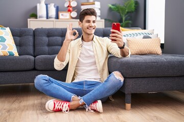 Sticker - Young hispanic man doing video call with smartphone doing ok sign with fingers, smiling friendly gesturing excellent symbol