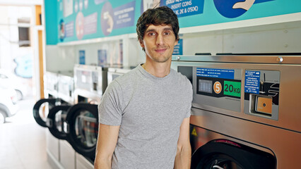 Poster - Young hispanic man smiling confident leaning on washing machine at laundry facility