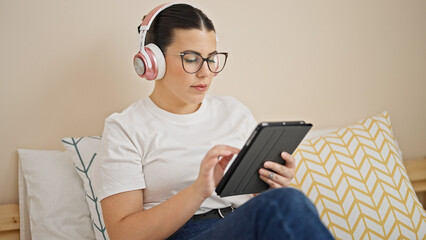 Canvas Print - Young beautiful hispanic woman using touchpad sitting on the bed wearing headphones at bedroom