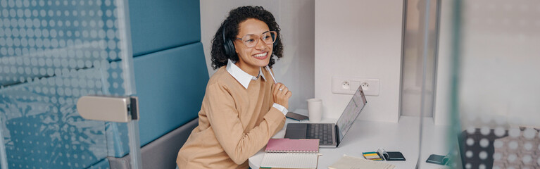 Wall Mural - Pretty female manager in eyeglasses working on laptop while sitting in modern office