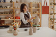 © Yaroslav Astakhov - Smiling young female ceramist wearing apron work with unfired clay vase in pottery studio