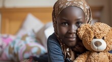 A Beautiful Girl Who Has Leukemia Sits On The Floor In Her Room Holding A Teddy Bear. Girl Undergoing Treatment For Leukemia Wearing A Headscarf And Smiling.