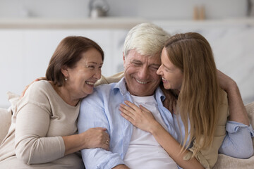 Wall Mural - Cheerful adult woman hugging older senior parents, smiling, laughing, chatting with mom and dad, having fun, enjoying relationship, affection, care. Family celebrating fathers day