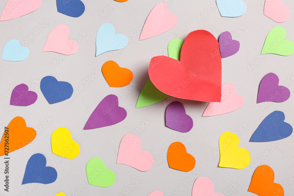 Red paper heart among colorful ones on grey background. Valentines Day celebration