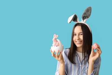 Poster - Pretty young woman with bunny ears, toy rabbit and Easter basket of eggs on blue background