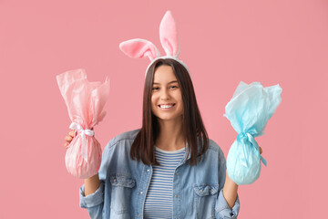 Poster - Pretty young woman with bunny ears and Easter gifts on pink background