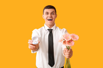 Wall Mural - Handsome man with flowers and engagement ring on yellow background