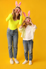 Poster - Cute little girl and her mother in bunny ears with painted Easter eggs on yellow background