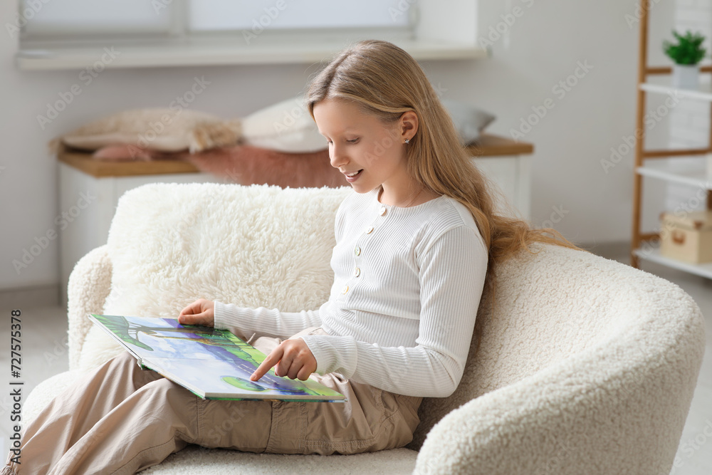 Little girl reading book on sofa at home