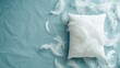 Soft white pillow amidst scattered feathers on blue backdrop