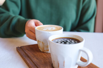 Wall Mural - Closeup image of a woman holding and drinking coffee with friend in cafe