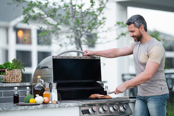 Wall Mural - Barbecue concept. Middle aged hispanic man in t-shirt for barbecue. Roasting and grilling food. Roasting meat outdoors. Barbecue and grill. Cooking meat in backyard.