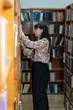 Young female student making order on bookshelves in college, woman student picking literature for education checking information in books store
