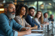 © pprothien - A thoughtful senior professional with a gray beard actively listens at a team meeting with multiethnic colleagues in the background.