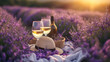 Two glasses of white wine and a bottle on background of a lavender field. Straw hat and basket with flowers lavender on a blanket on picnic. Romantic evening in sunset rays. Summer in Provence, France
