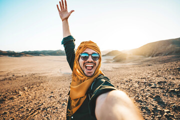 Wall Mural - Happy traveler with backpack taking selfie picture with smart mobile phone outdoors - Cheerful guy smiling on the top of the mountain - Hiker traveling in rocky desert - Travel technology life style