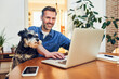 © baranq - Happy man at home using laptop sitting together with his dog