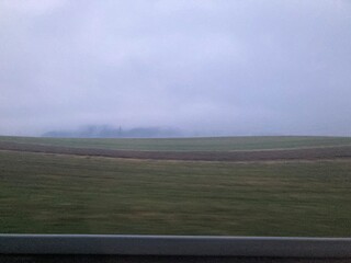 Poster - Serene countryside landscape featuring a spacious green meadow with a barn in the far distance