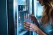 A woman is seen holding a glass of water in front of a refrigerator. This image can be used to depict a healthy lifestyle and hydration