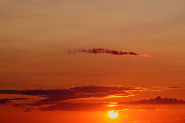 Wall Mural - The evening sky is filled with hues of orange and red, as the sun sets behind the horizon, casting a warm glow over the landscape.