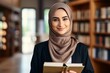 © Sunny - A young Muslim woman with her head covered stands in the library among books. Islamic education concept for women