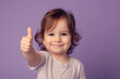 © TimeaPeter - Joyful Gesture: Cute Brunette Toddler Expresses Positivity with Thumbs Up on Purple Background