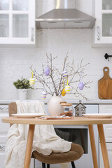 Home spring easter design in kitchen. Ceramic vase with spring branches with easter eggs, plates for two person in white kitchen. High quality photo.