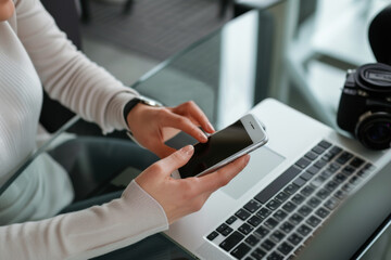 Poster - A woman is using a cell phone next to a laptop