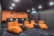 © alhim - The interior of a home theater with gray walls and flooring. A large grey sofa and orange armchairs.