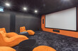 © alhim - A stylish home theater with gray decor, a huge screen and ergonomic orange chairs.