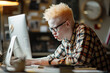 © ivlianna - Young albino man studying in a university library for his exam. Albino student is sitting behind his desk and working on a personal computer reading school materials.