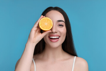 Poster - Beautiful young woman with piece of orange on light blue background