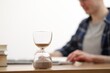 © New Africa - Hourglass with flowing sand on desk. Man taking notes indoors, selective focus