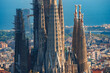 Closeup of Sagrada Familia's spires in Barcelona, showcasing Gaudi's Gothic and Art Nouveau design, with cranes indicating ongoing construction against a cityscape backdrop.