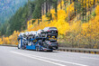 Professional industrial car hauler big rig semi truck transporting car on two level modular semi trailer driving on the wide highway road with autumn trees on the mountain hills in Columbia Gorge