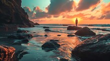 A Serene Beach Scene At Sunset With Warm Colors Filling The Sky, Reflected Off Wet Sand And Rocks. A Single Person Stands On A Larger Rock To The Right, Silhouetted Against The Vibrant Backdrop Of The