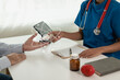© MrAshi - Provide medical consultation Doctor talking with patient in clinic office Focus on the hand and stethoscope Doctor and patient sit and talk with patient about medication. At the table by the window