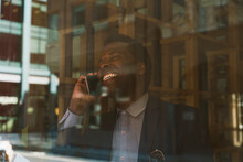 Happy Businessman Talking On Smart Phone Seen Through Glass