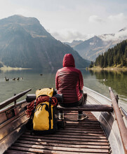 Young Woman With Backpack Sitting In Boat At Lake Vilsalpsee Near Mountains, Tyrol, Austria