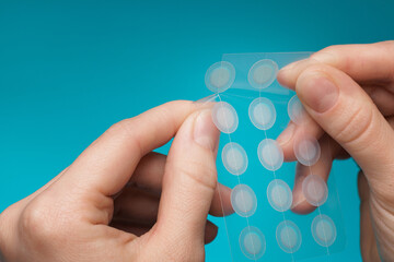 close-up round acne patch on finger on blue background. acne patches for treatment of pimple and ros