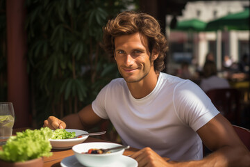 Wall Mural - Male tennis player tastes vegan dishes on restaurant terrace. Healthy food provides sportsman with nourishment to peak performance on court