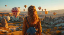Young Woman Watch Sunrise With Hot Air Balloons Flying Over Love Valley With Rock Formations And Fairy Chimneys In Cappadocia Turkey