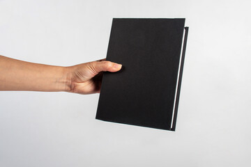 Wall Mural - Blank black book cover in hand on white background.