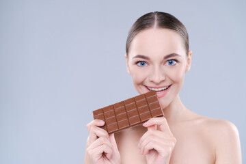 Wall Mural - Close up beautiful girl biting chocolate bar joyfully on white background, studio shot.