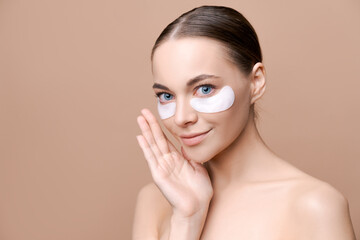 Wall Mural - portrait smiling cheerful beautiful woman posing with under eye hydrogel patches skin care, morning routine. Indoor studio shot over beige background.