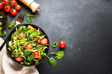 Wall Mural - Green Salad with salad leaves and vegetables at black background.