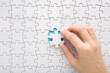 © fotoduets - Young adult woman hand holding and putting last one white puzzle piece in middle on blue table background. Closeup. Top down view.