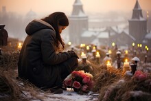 In A Poignant Moment, A Woman Sits Beside A Grave Adorned With Flowers, Paying Heartfelt Tribute To A Departed Loved One.